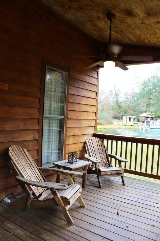 Covered wooden porch with two rocking chairs, ceiling fan, and view of a yard beyond the railing