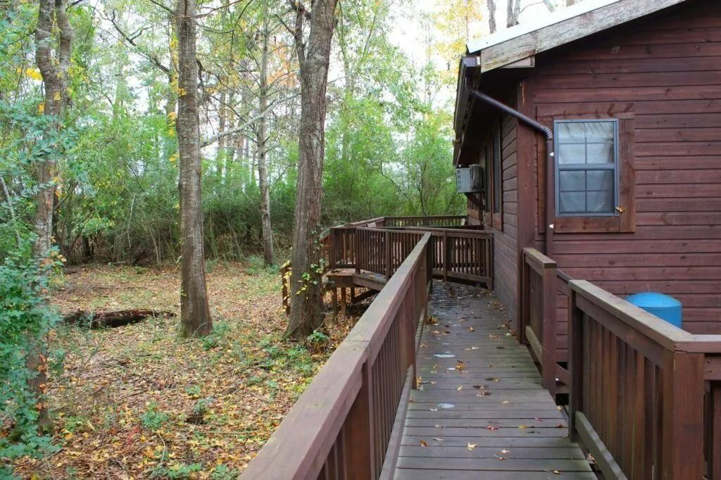 Wooden deck beside a brown cabin in a wooded yard with autumn leaves.
