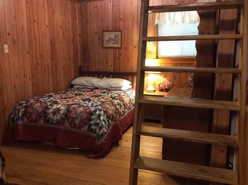 Cozy wood-paneled bedroom with a bed, floral quilt, and loft ladder