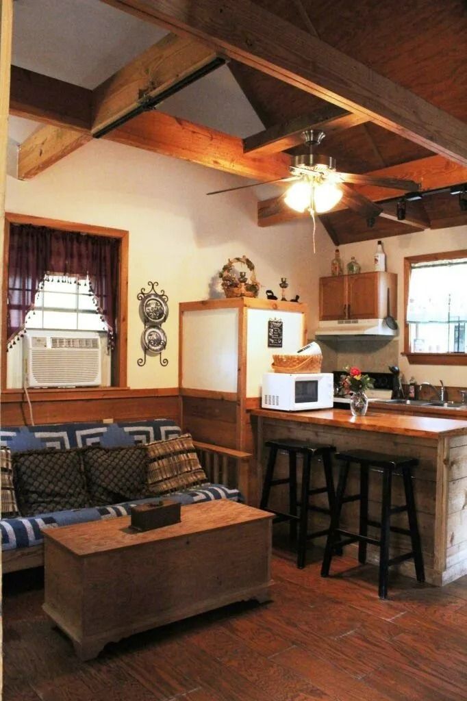 Cozy cabin living room with exposed beams, couch, wood stove, and breakfast bar kitchen area