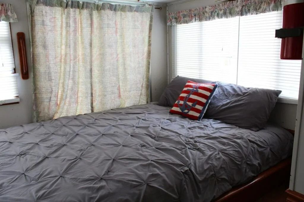 Bedroom with a neatly made bed, gray comforter, striped pillow, and floral curtains by bright windows
