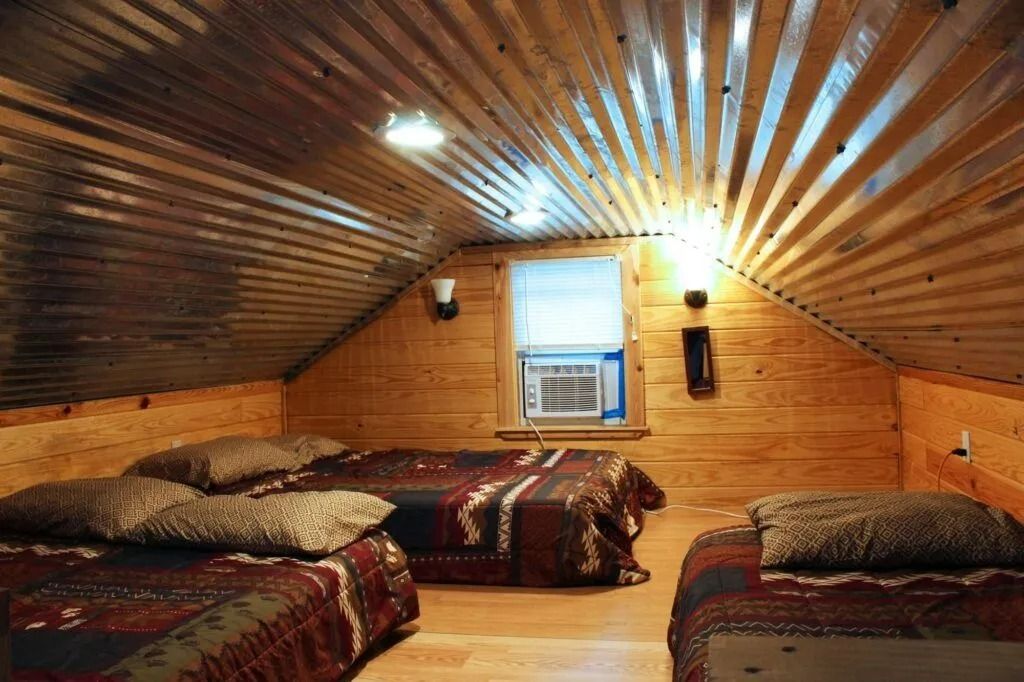 Cozy attic bedroom with wood-paneled walls, three beds, and a small window under a sloped ceiling