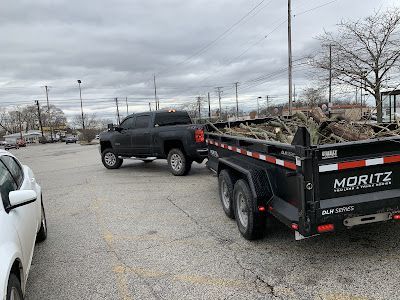 A truck is towing a dumpster in a parking lot.