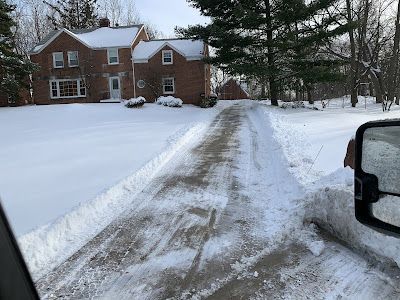 A snowy driveway leading to a large brick house.