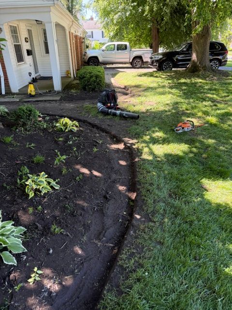 Backyard landscaping with a curved mulch bed, green lawn, and a person working near the house.