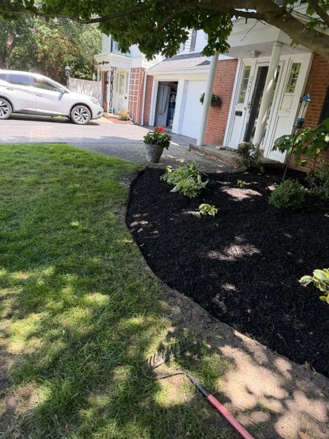 Front yard landscaping with dark mulch bed, green lawn, and a house with white trim and driveway.