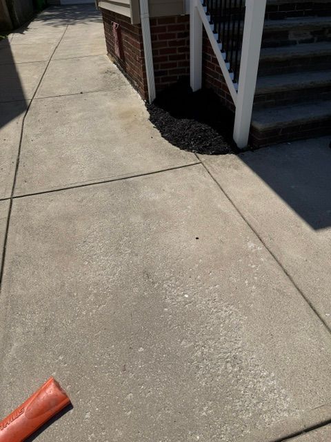 Concrete sidewalk beside a brick house and stairs, with a red object at the lower left.