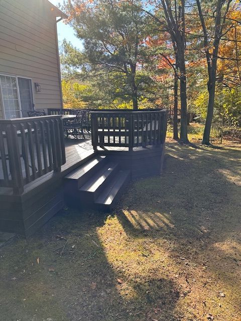 Wooden deck with stairs next to a house, surrounded by grass and trees with fall foliage.
