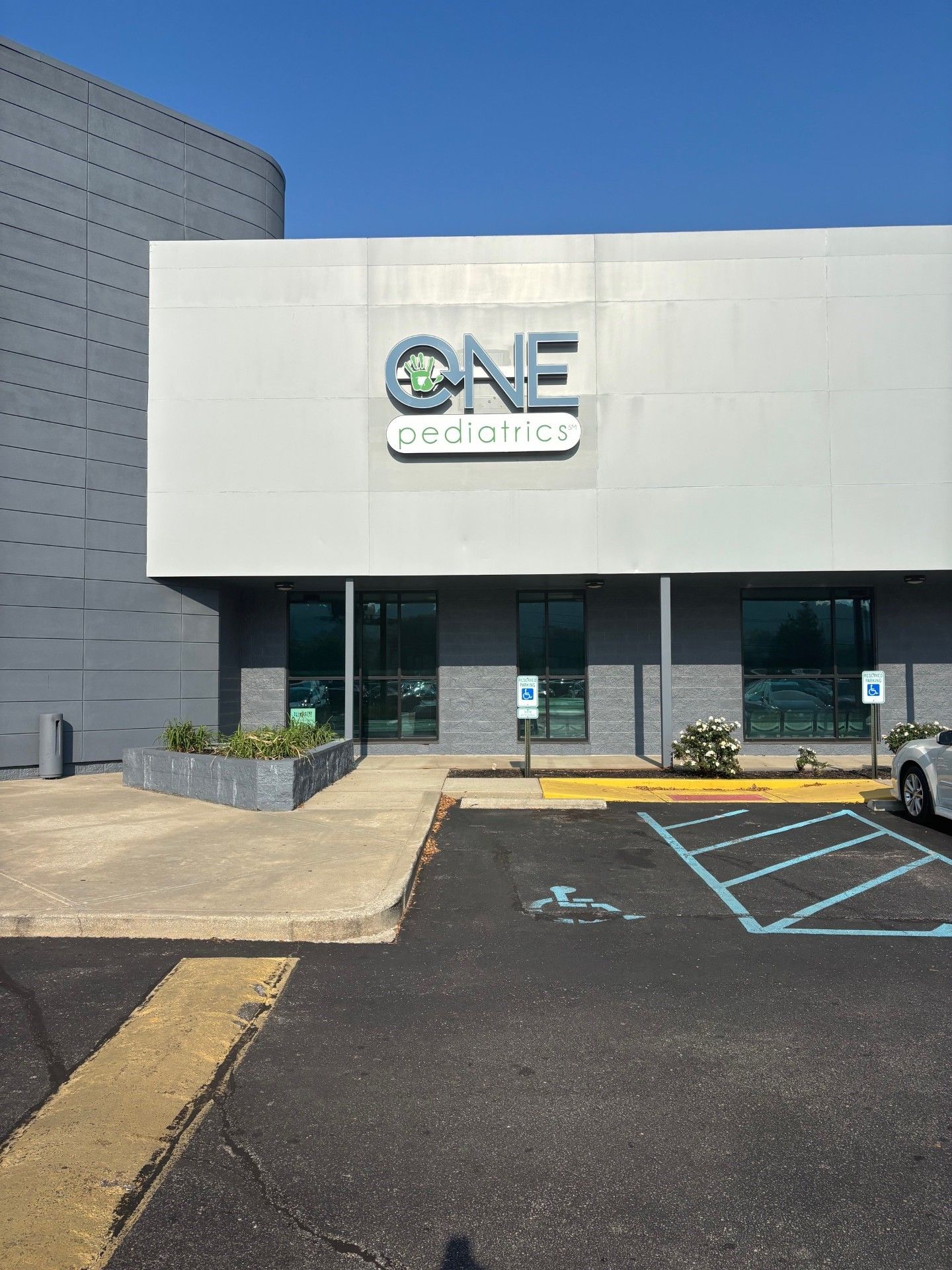 Exterior of a building: "ONE pediatrics" sign above entrance, accessible parking space in front.