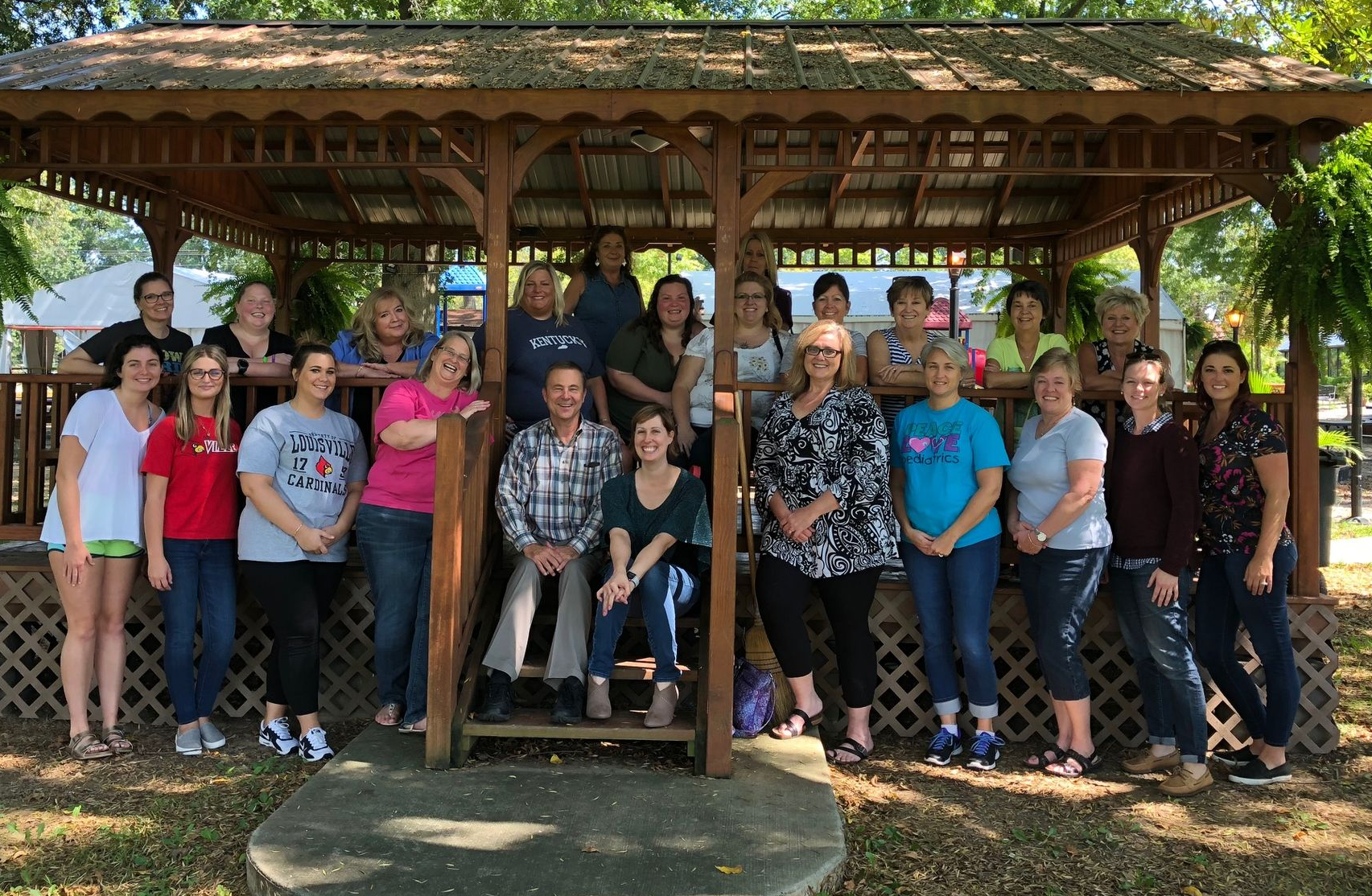 Group of people posing together on steps of a gazebo. Trees and a deck in the background.