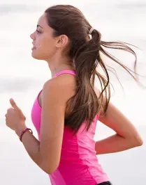 Woman in pink tank top running, hair in ponytail.
