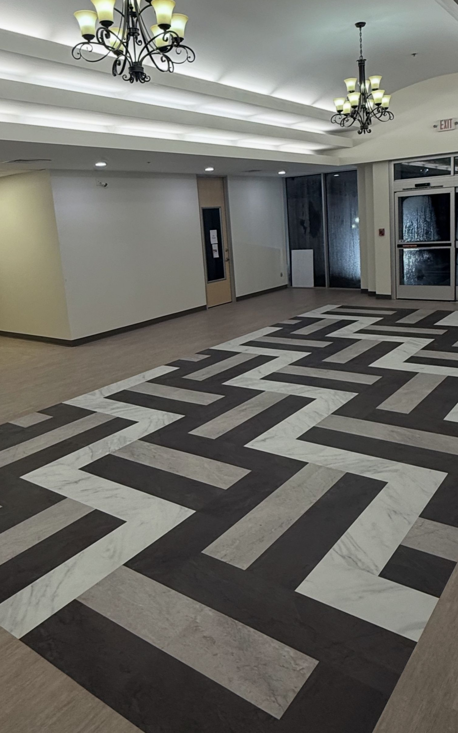 Lobby with geometric floor, white walls, and chandeliers. Entrance door on the right.