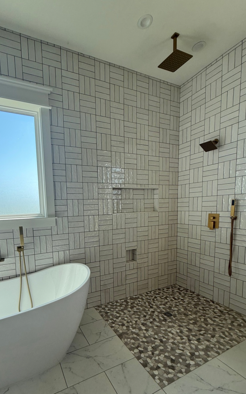 Modern bathroom with patterned tile walls, freestanding tub, and pebble shower floor.