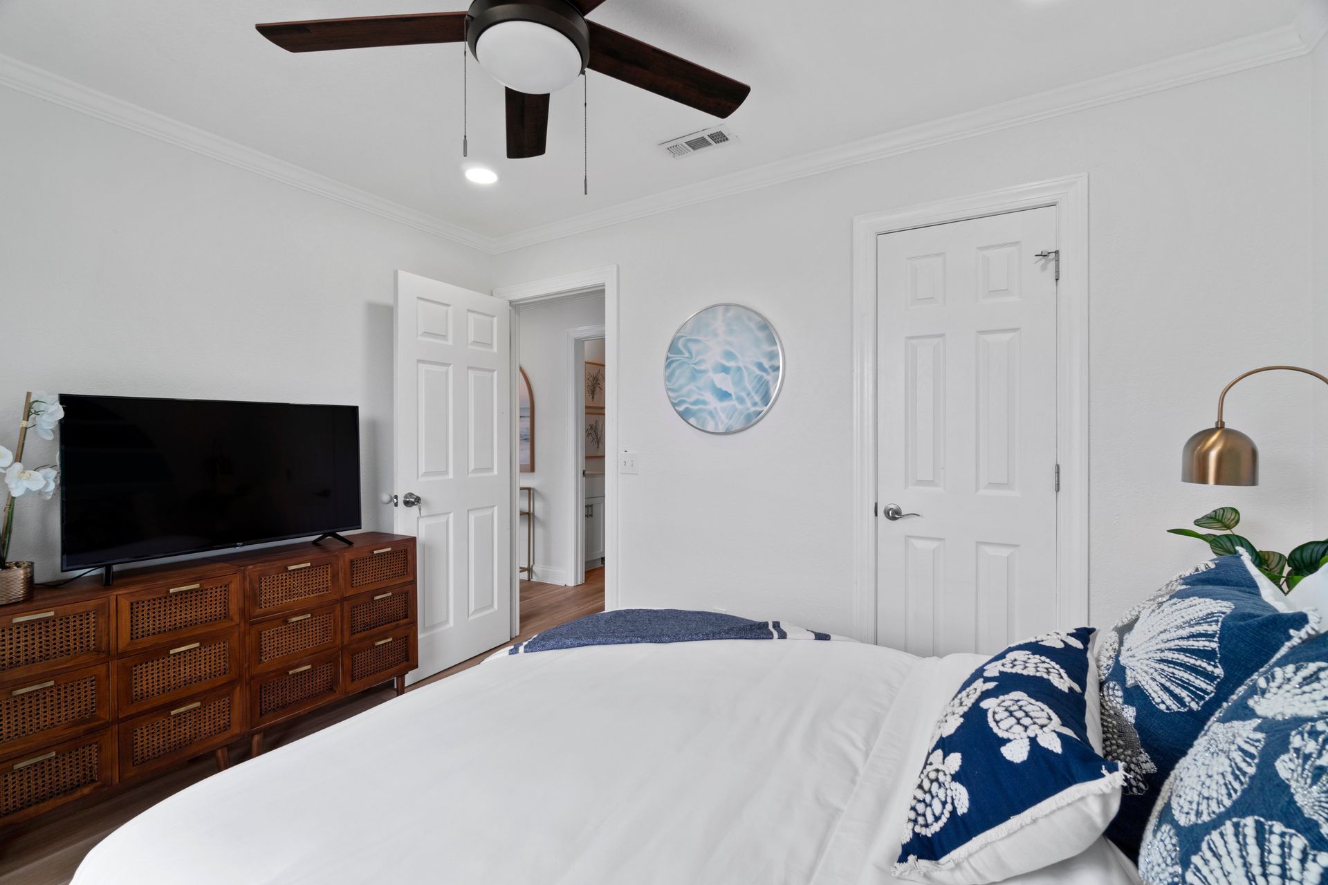 Bright bedroom with white walls, navy patterned bedding, dresser, TV, and ceiling fan
