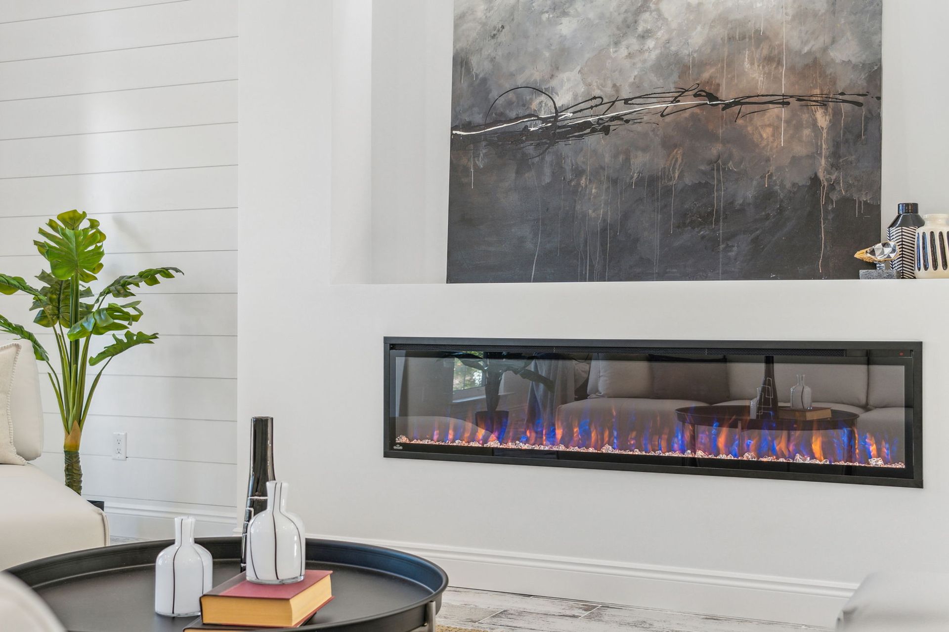 Modern living room with long linear fireplace, abstract wall art, plant, and round coffee table