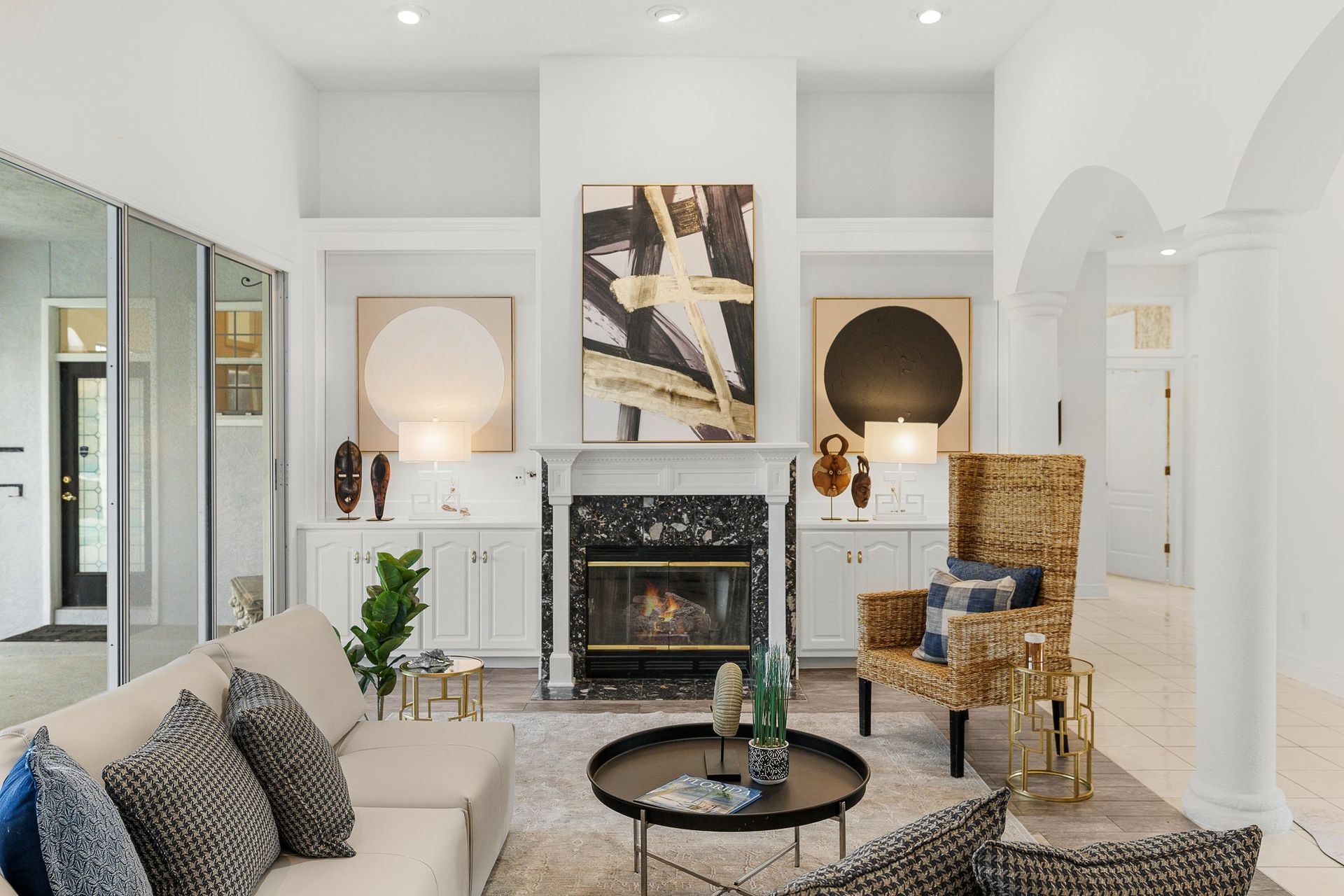Bright living room with fireplace, mirrored walls, patterned chairs, and a black coffee table