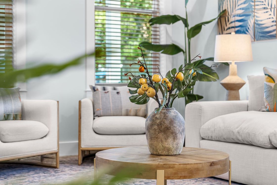 Bright living room with white chairs, a round wood table, and a vase of yellow flowers by a window
