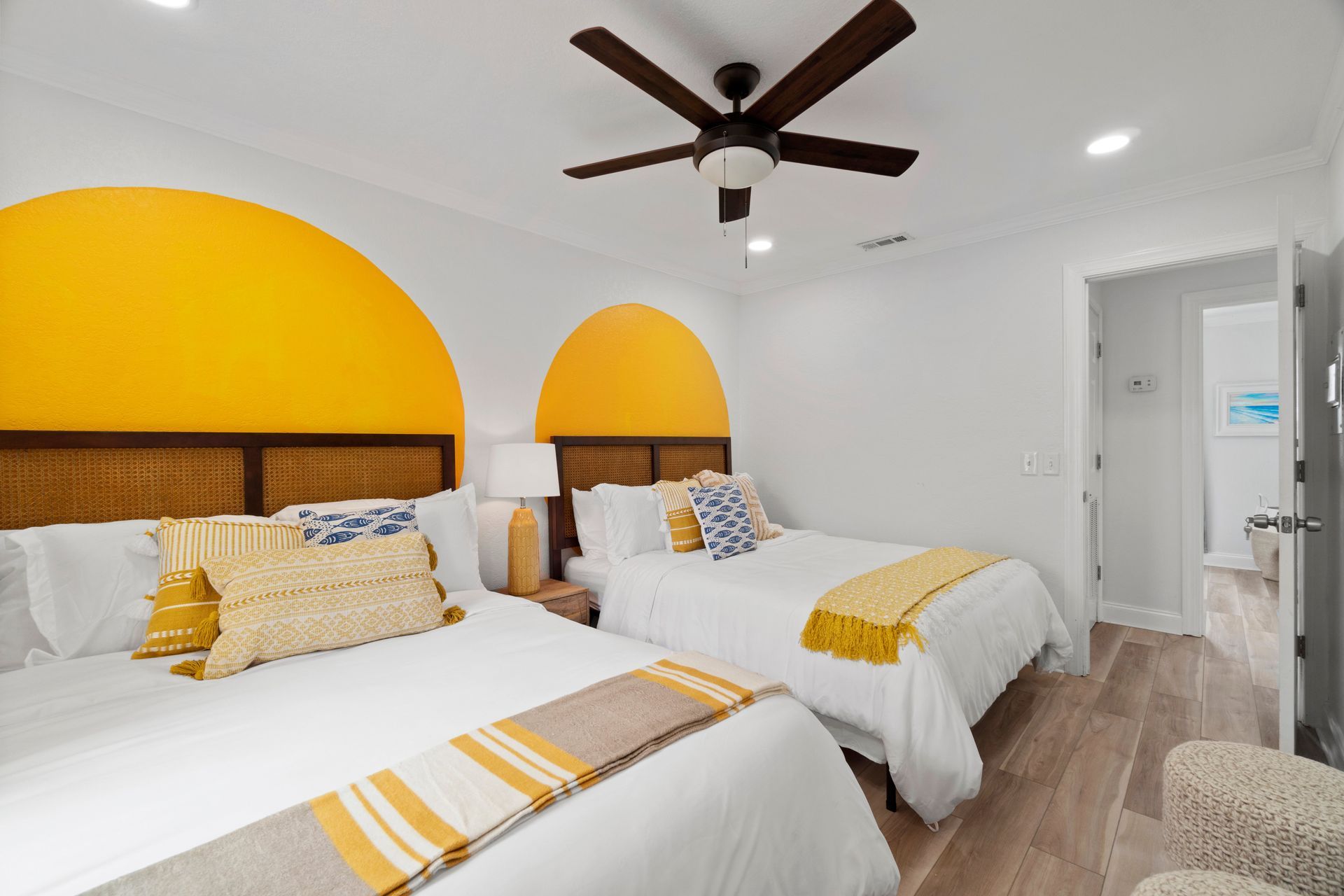 Bright bedroom with two beds, yellow accent walls, ceiling fan, and a white door