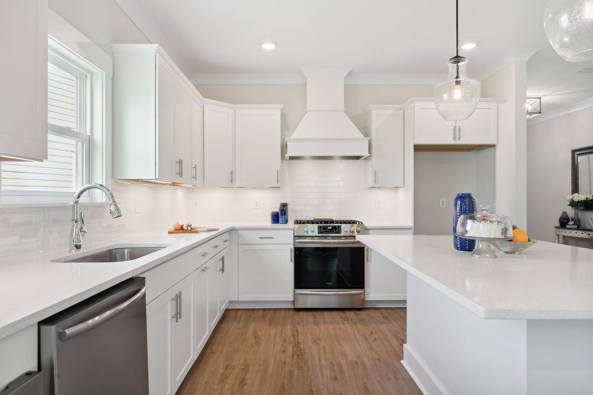 Bright white modern kitchen with island, stainless steel stove, and wood floor