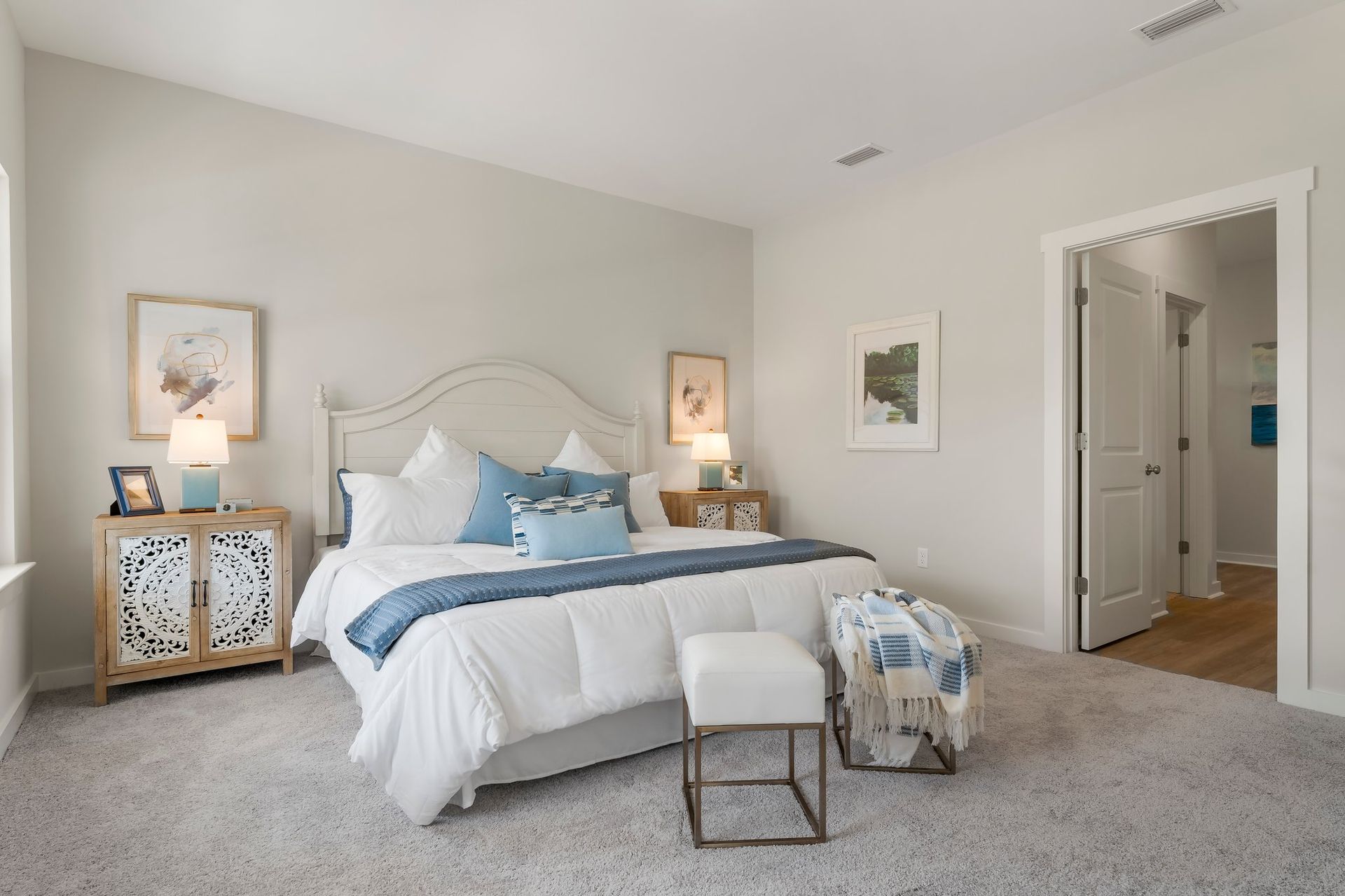 Bright, airy bedroom with white bed, blue accents, patterned nightstands, and an open doorway to the hall.