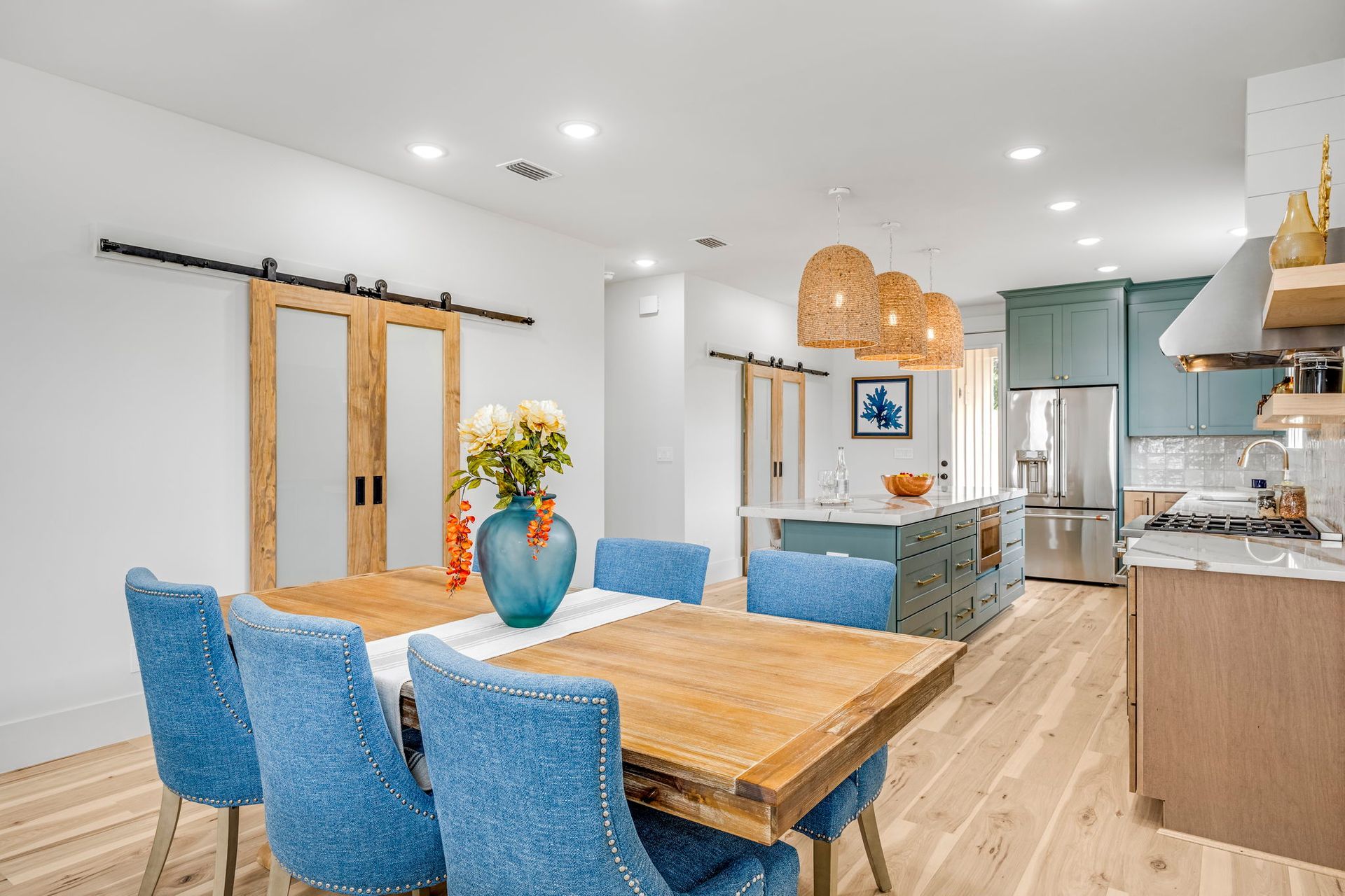 Bright modern kitchen and dining area with blue chairs, wood table, and open layout to living room