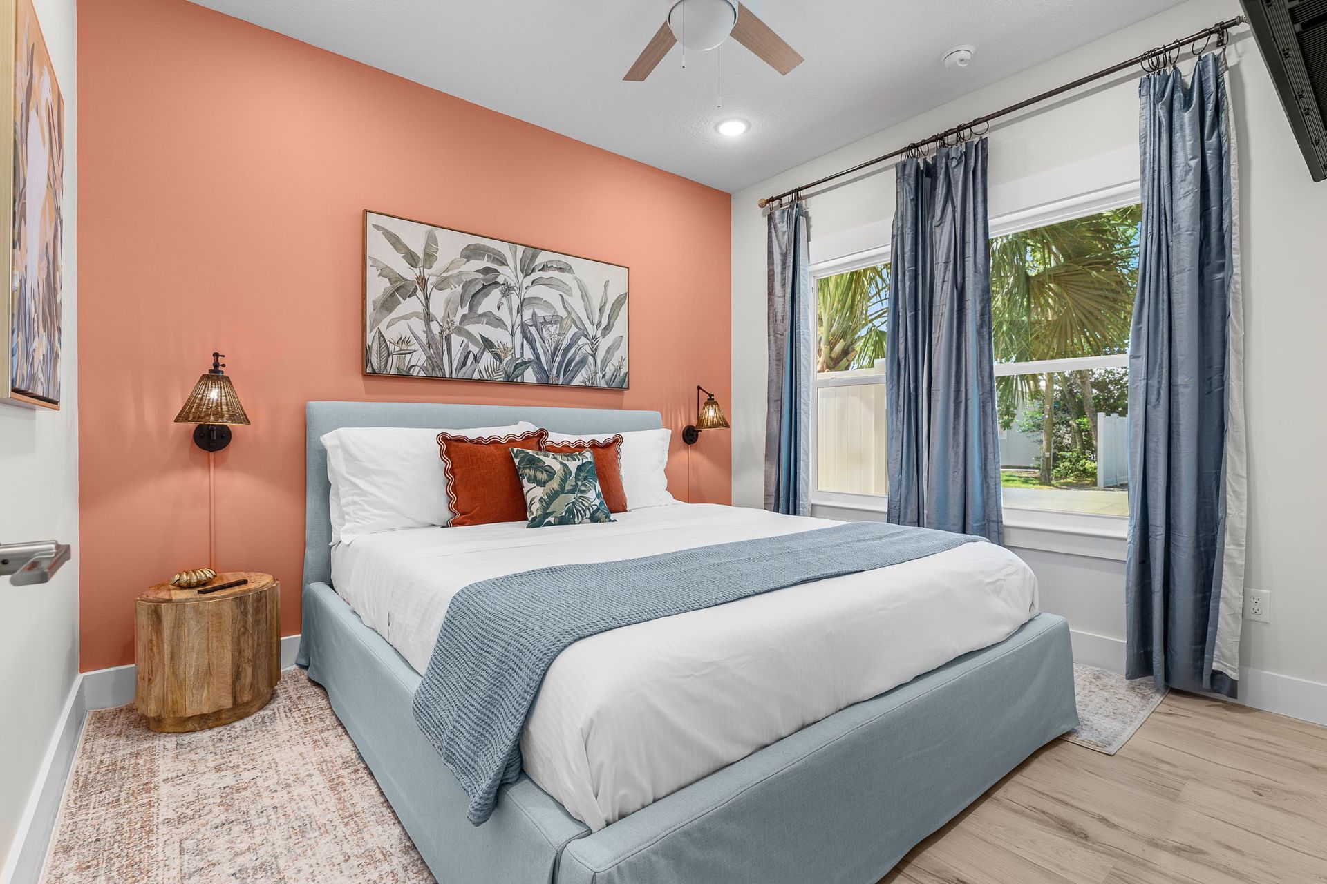 Cozy bedroom with coral accent wall, white bedding, blue throw, and large window with curtains
