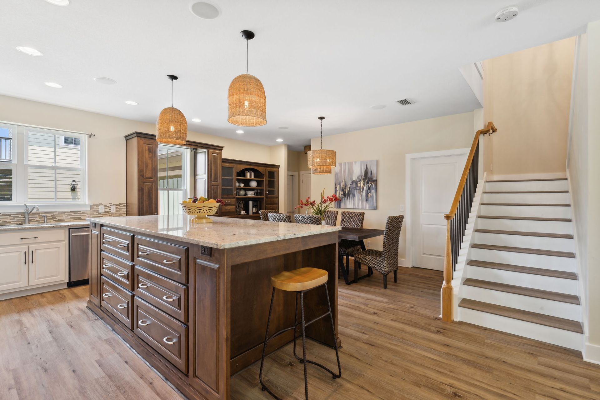 Bright modern kitchen with large island, pendant lights, wood floors, and staircase to the right