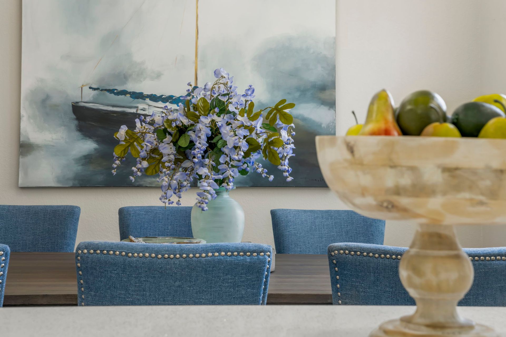 Dining room with blue chairs, a vase of purple flowers, and a fruit bowl on the table