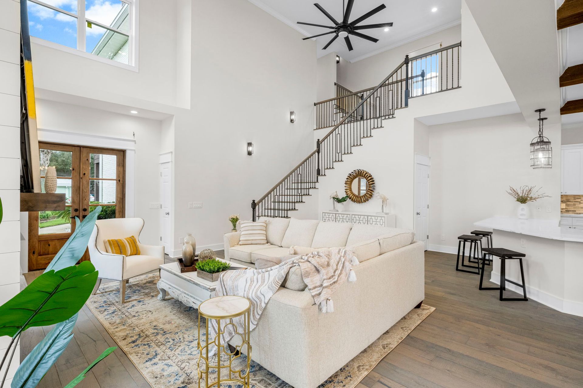 Bright modern living room with white sectional sofa, staircase, high ceilings, and large windows