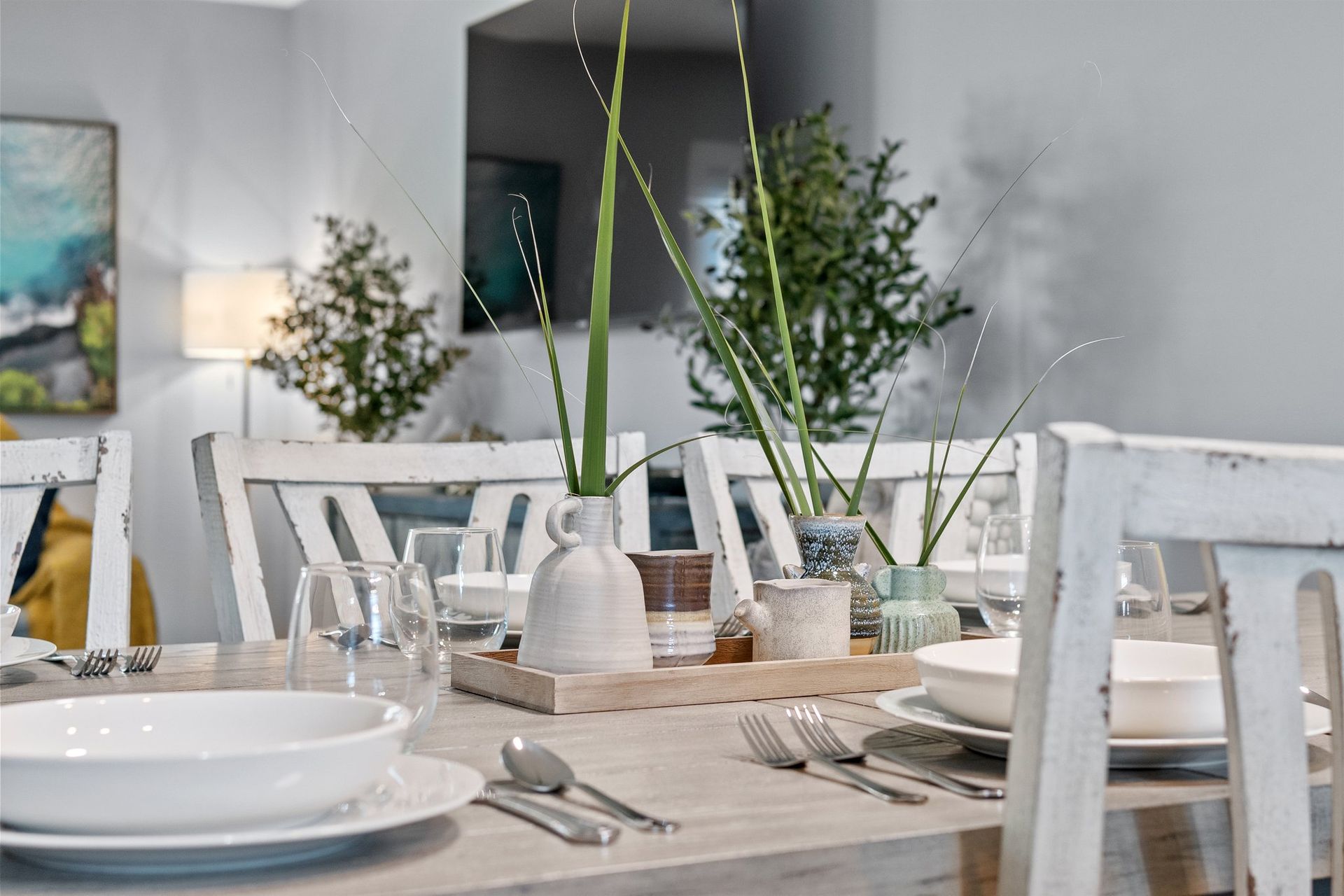 Bright dining table set with white dishes, glassware, and tall green stems in a modern room