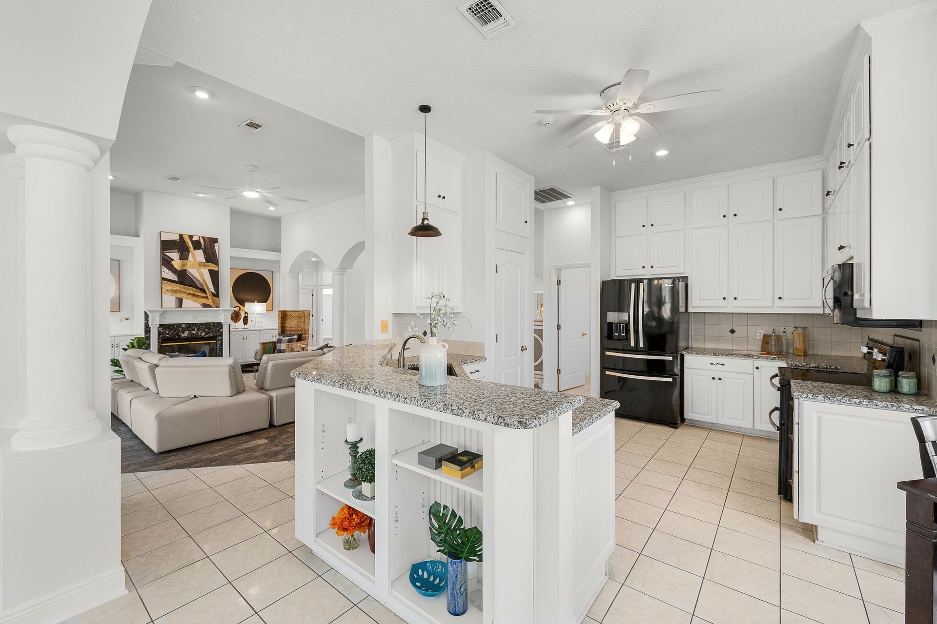 Bright white kitchen with island, tiled floor, and adjacent living area with sofa and wall art