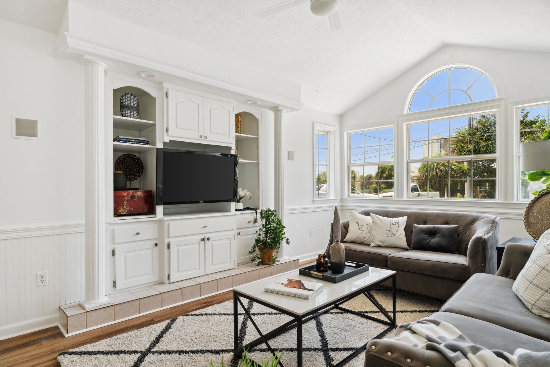 Bright living room with white built-ins, a sofa, coffee table, and large arched window.