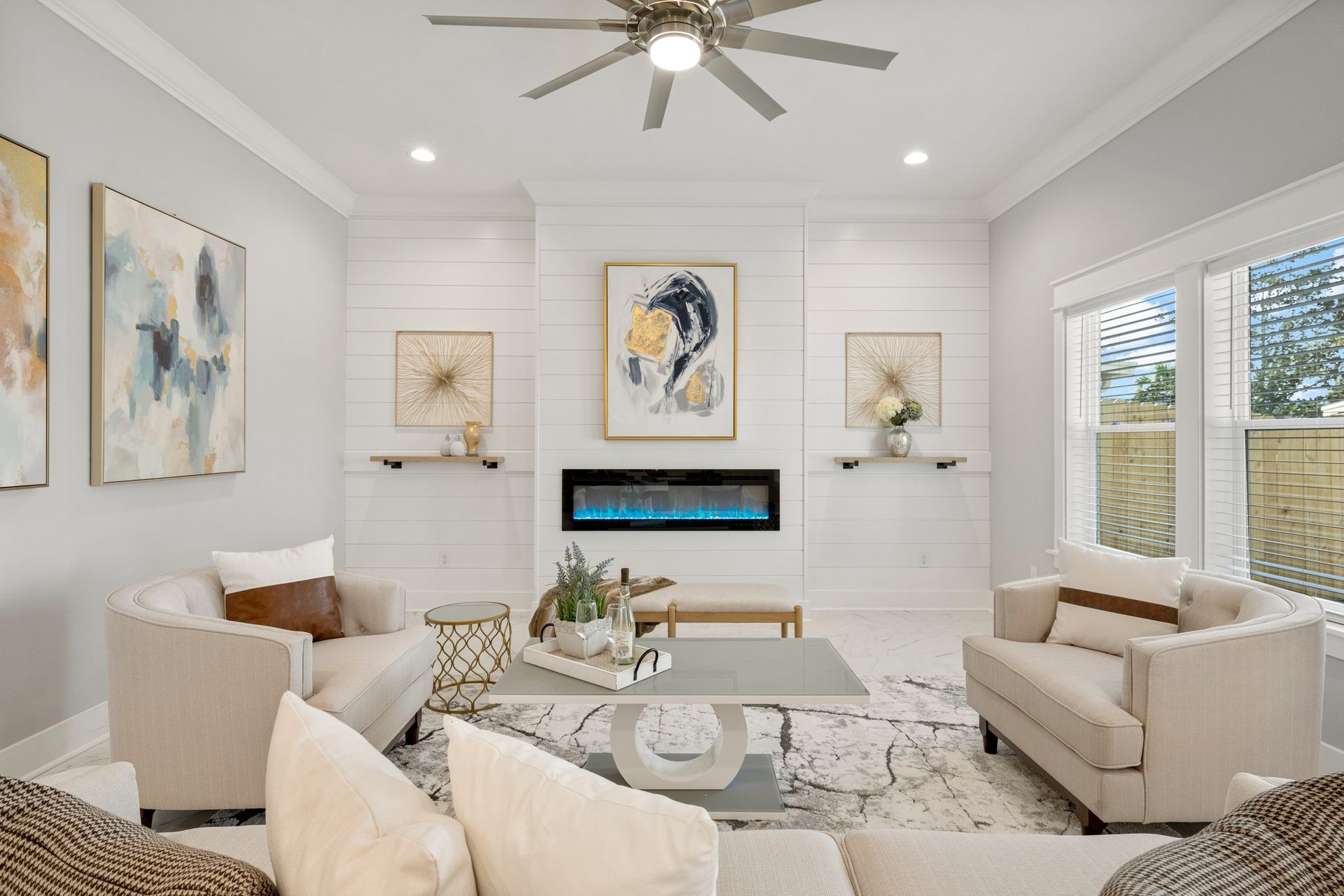 Bright modern living room with cream furniture, fireplace, artwork, and large windows