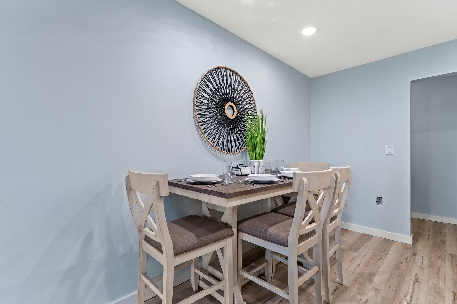 Dining nook with wooden table and chairs, light blue walls, and a decorative wall piece.