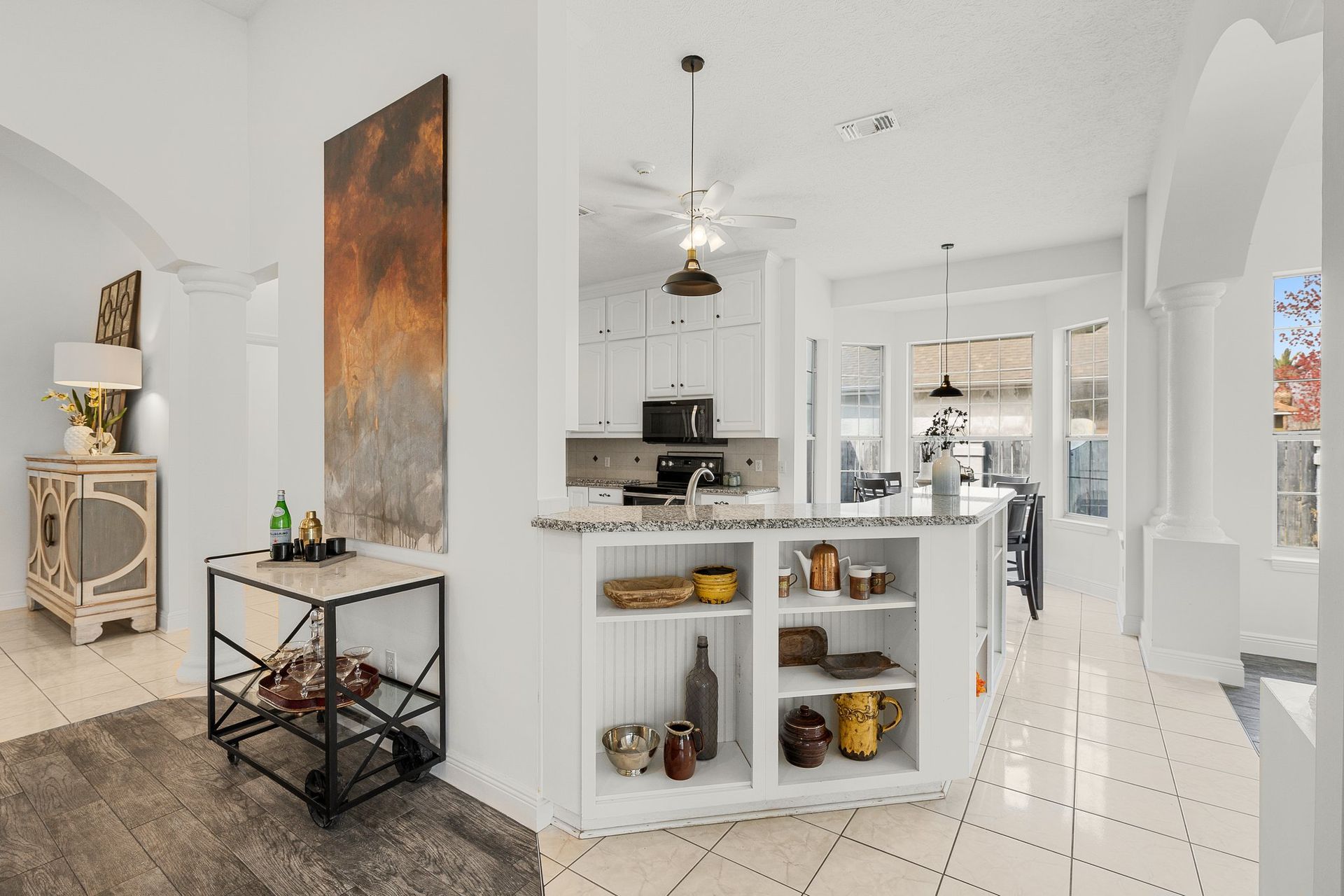 Bright open kitchen and dining area with white walls, tiled floor, island shelves, and modern decor