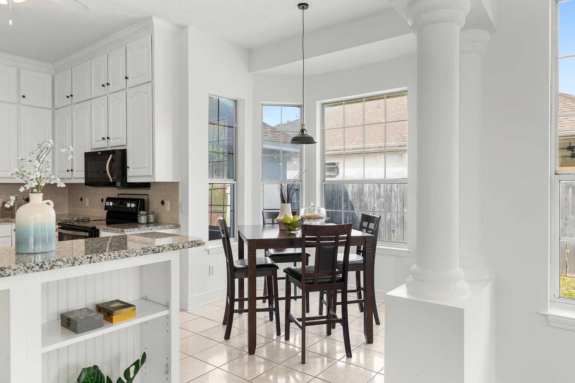 Bright white kitchen opening to a dining area with a dark wood table and chairs by large windows
