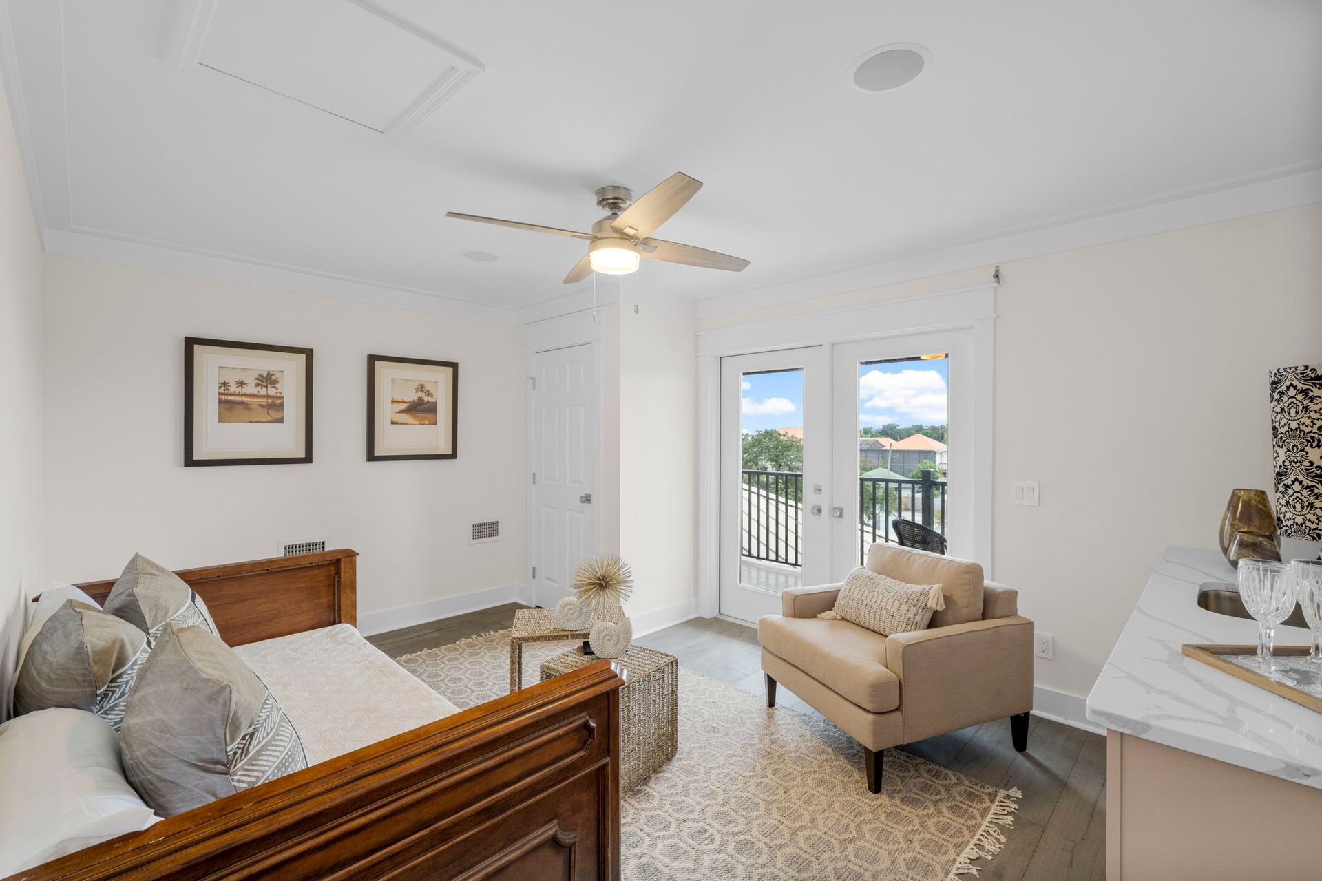 Bright bedroom with twin beds, cream seating, framed art, and balcony doors to a sunny view.
