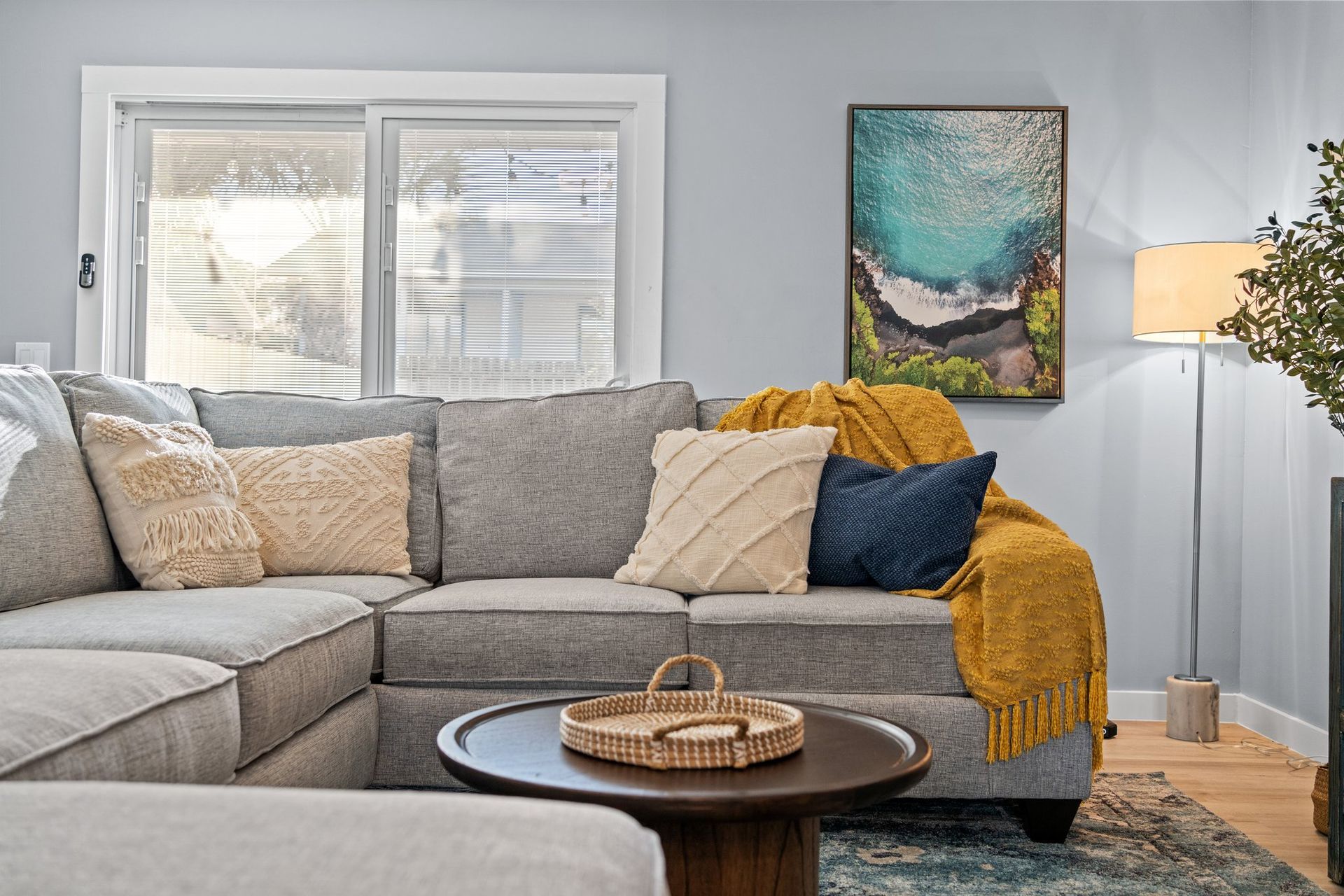 Cozy living room with gray sectional, beige pillows, mustard throw, round coffee table, and abstract wall art.