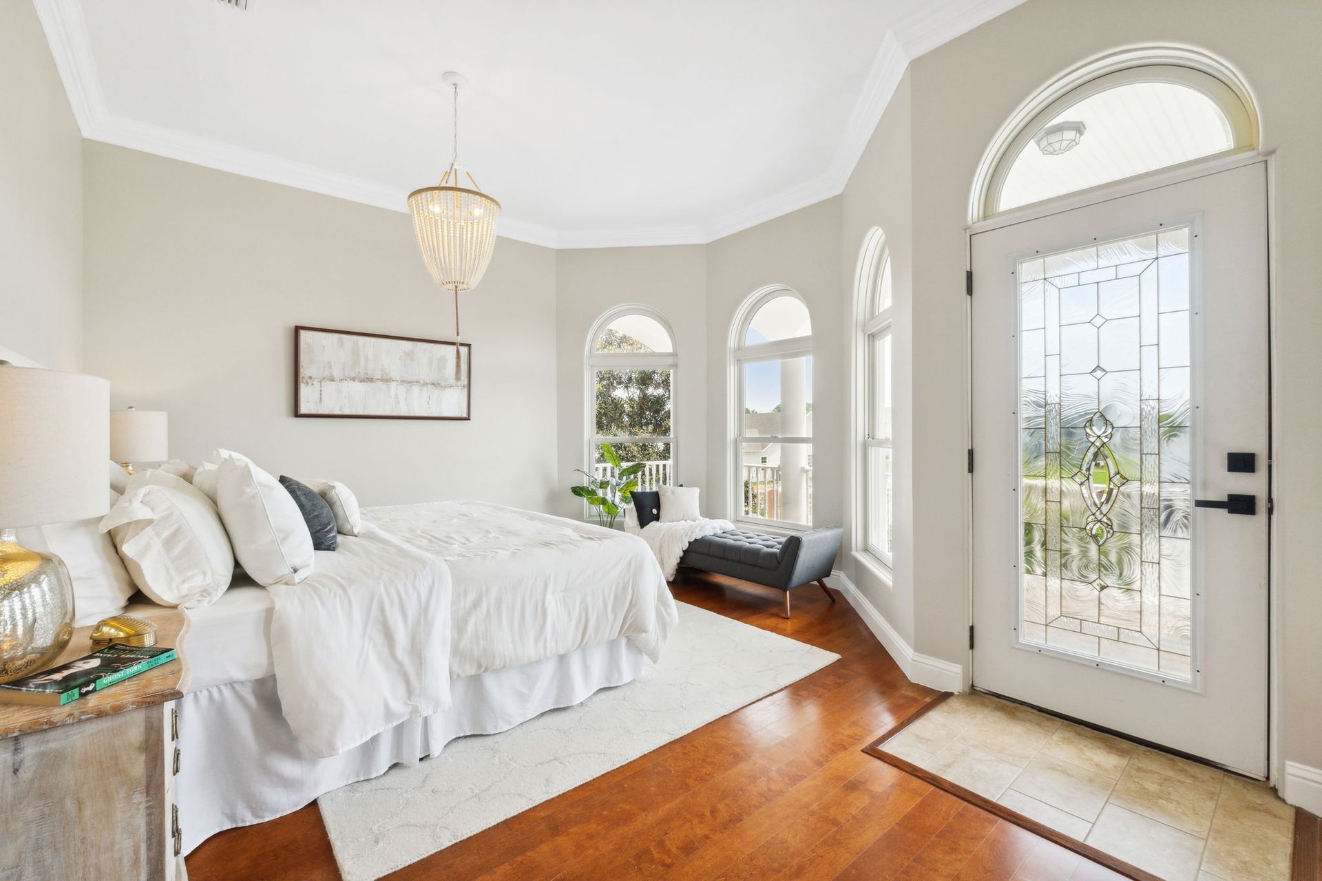 Bright bedroom with white bedding, hardwood floors, and arched French doors to a porch
