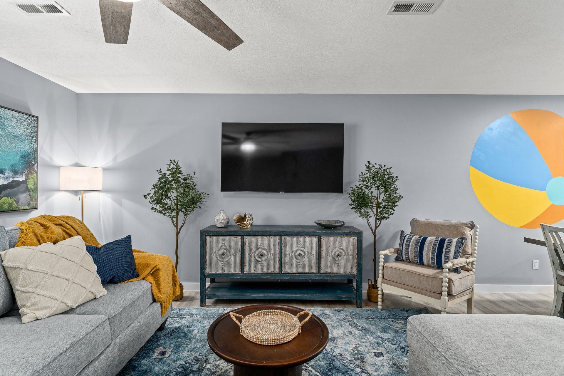 Modern living room with wall-mounted TV, blue rug, gray sofa, yellow throw, and striped armchair