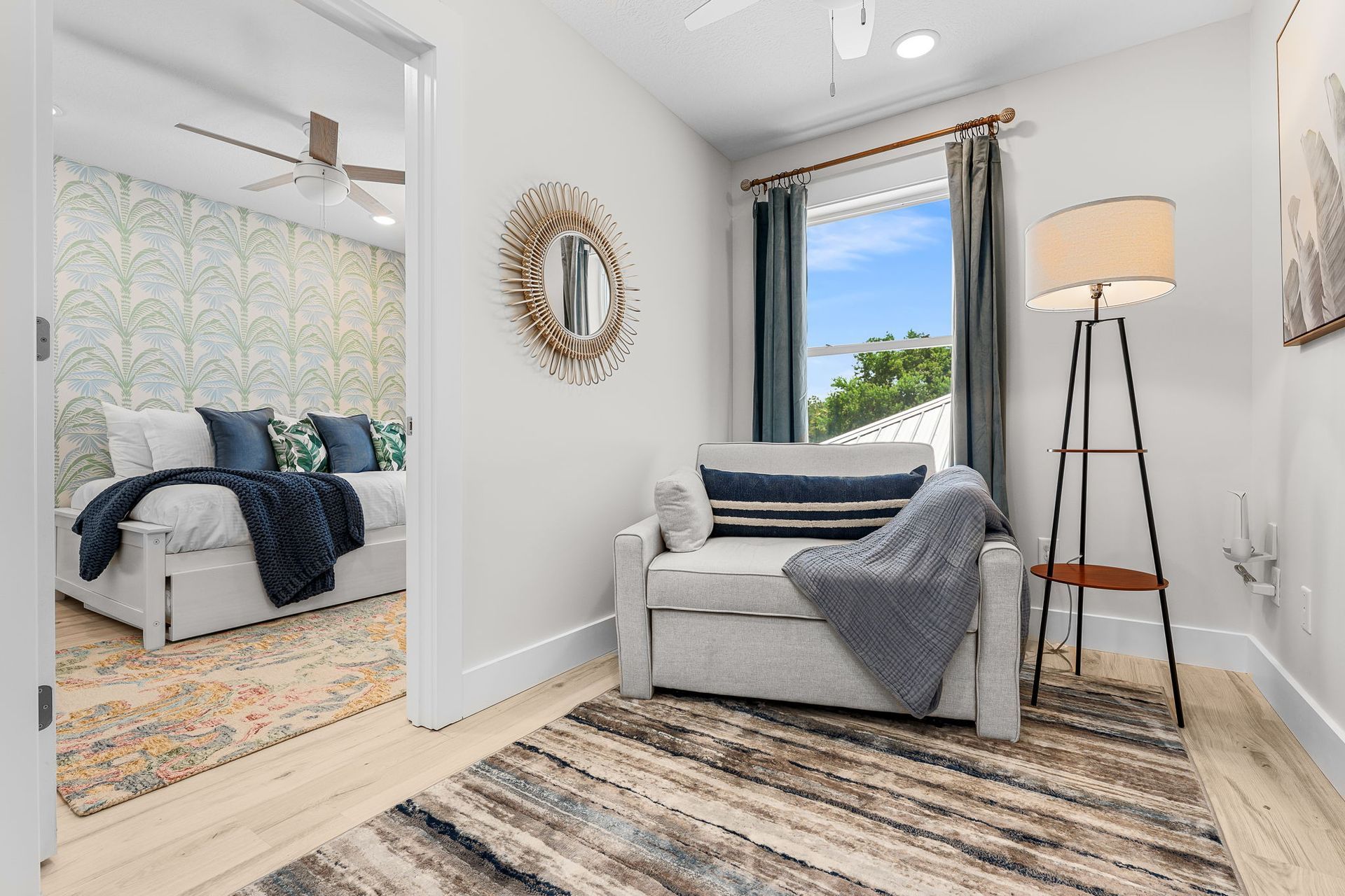 Bright white bedroom with a gray chair, striped rug, standing lamp, and mirrored accent wall