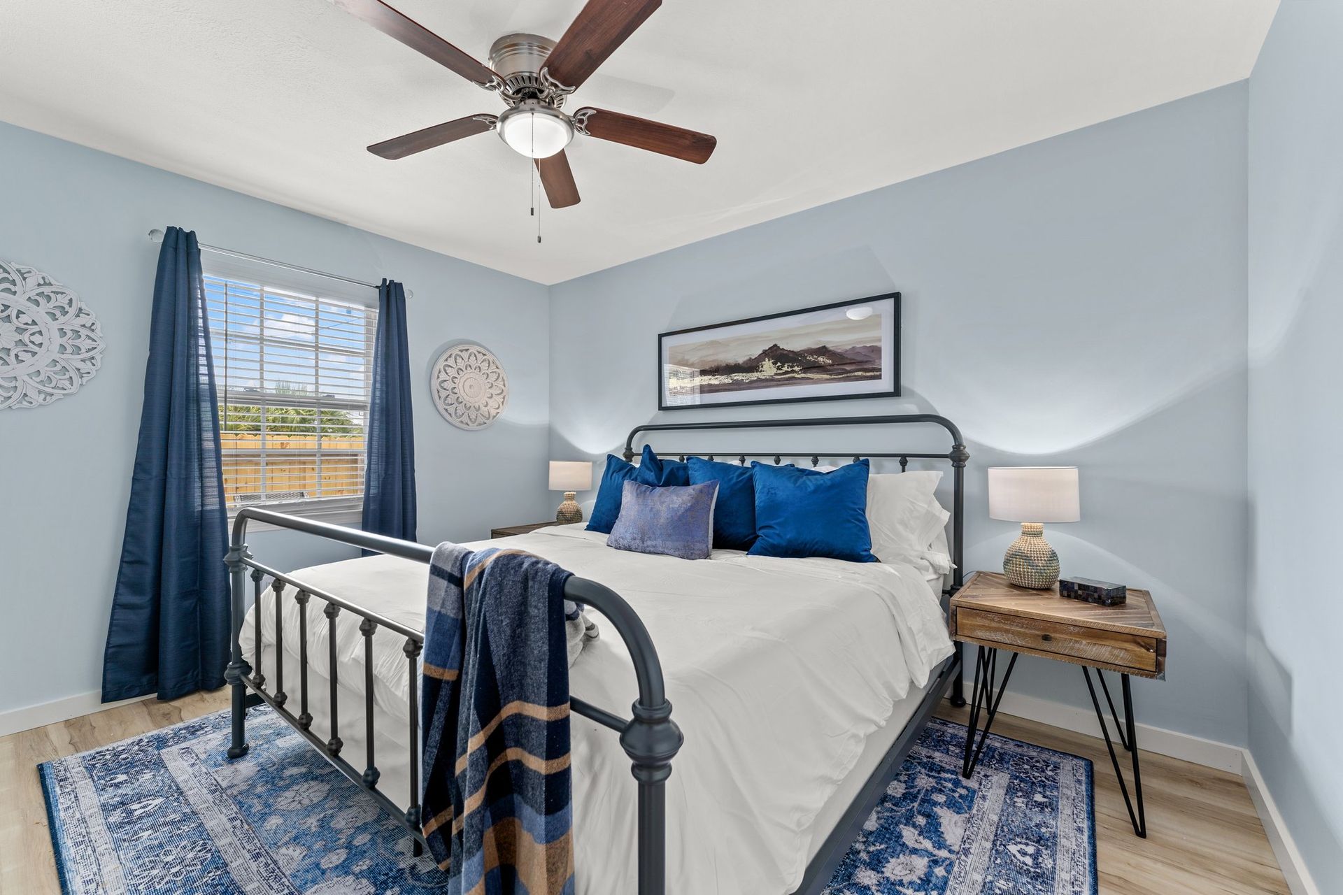 Blue bedroom with metal bed frame, ceiling fan, window, and patterned rug