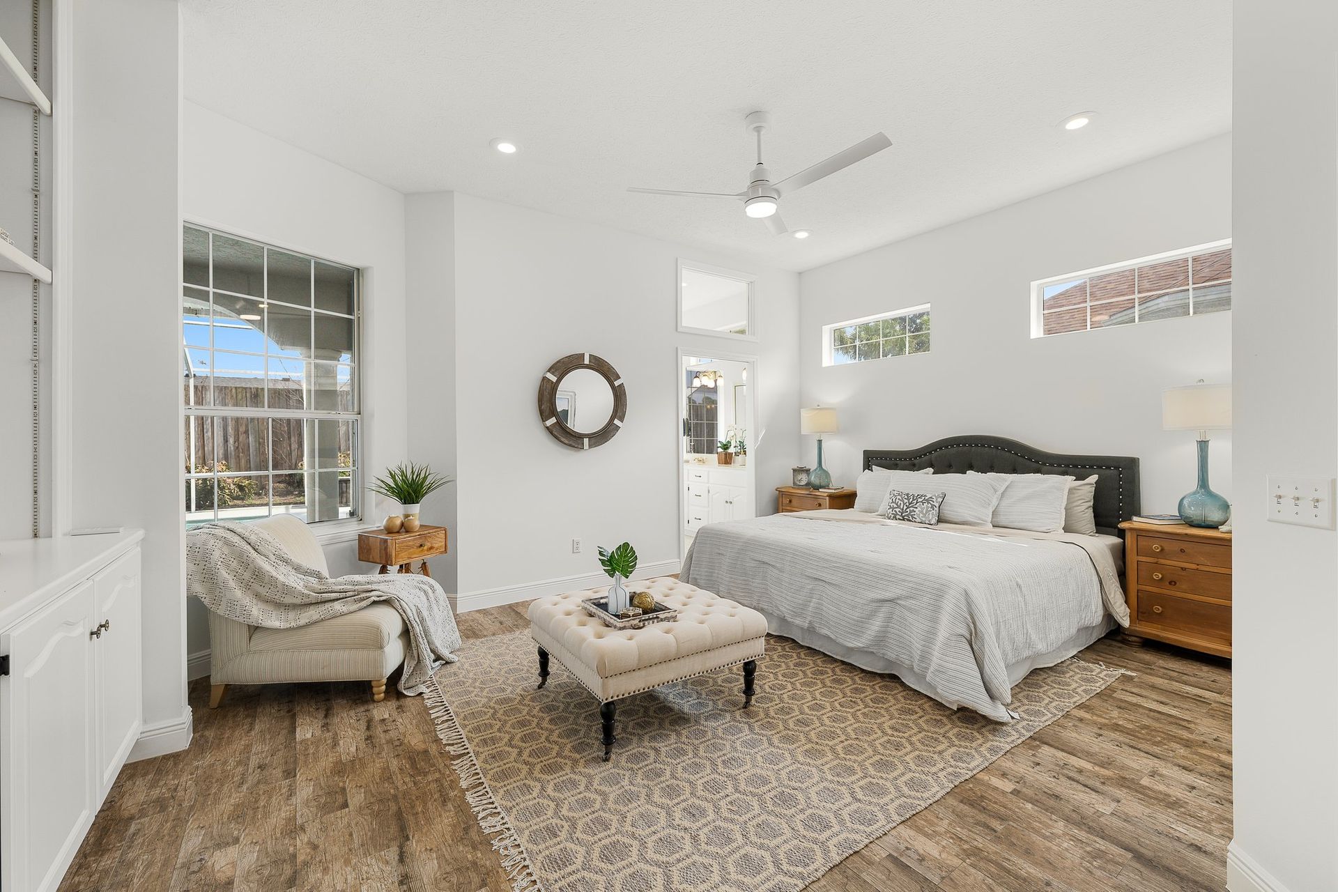 Bright airy bedroom with white walls, gray bed, wicker chair, and tan rug.