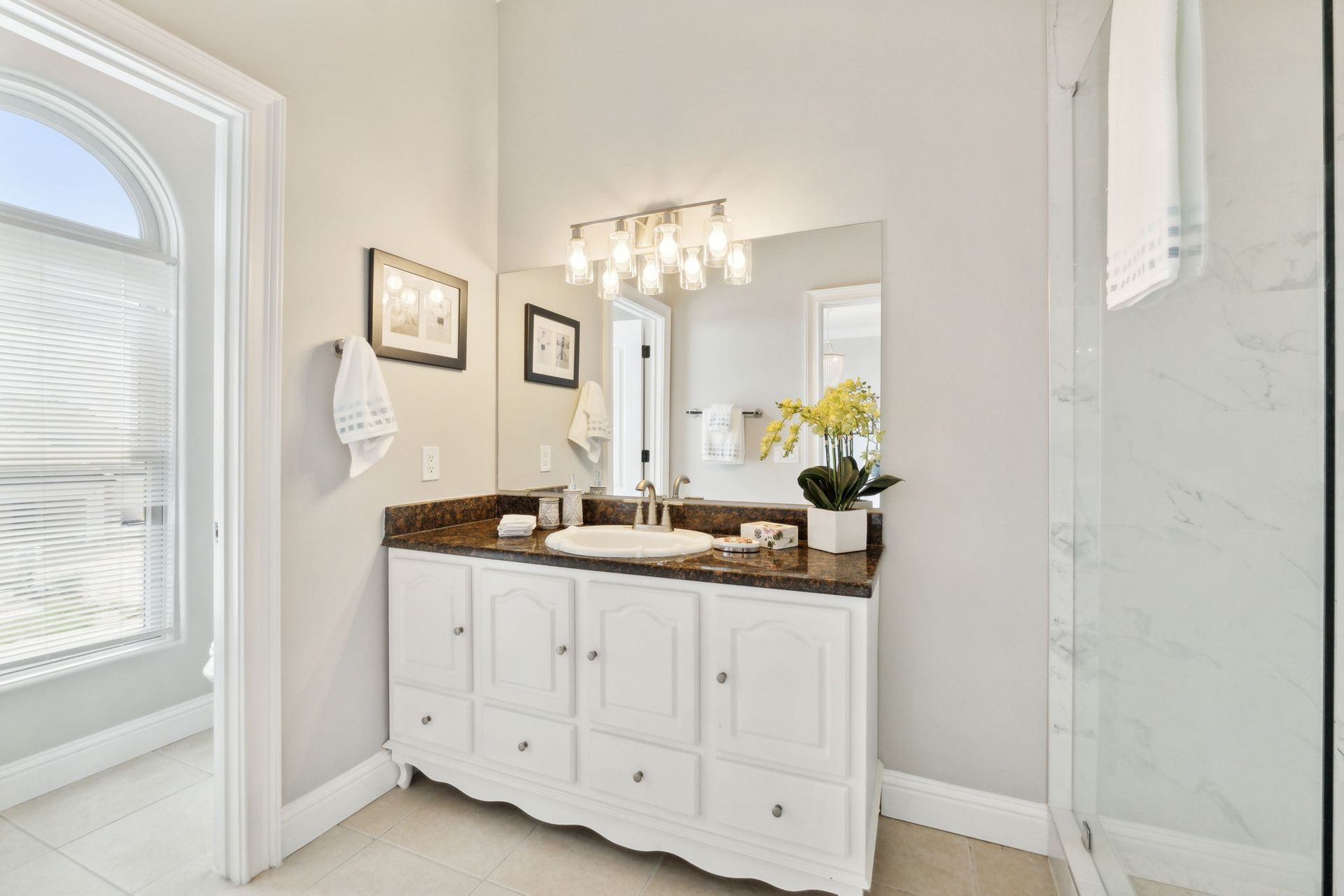 Bright bathroom vanity with white cabinets, granite countertop, mirror, and yellow flowers beside a window
