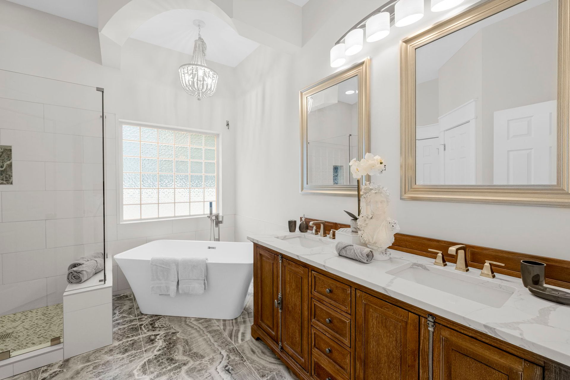 Bright white bathroom with freestanding tub, double vanity, large mirrors, and patterned floor tiles