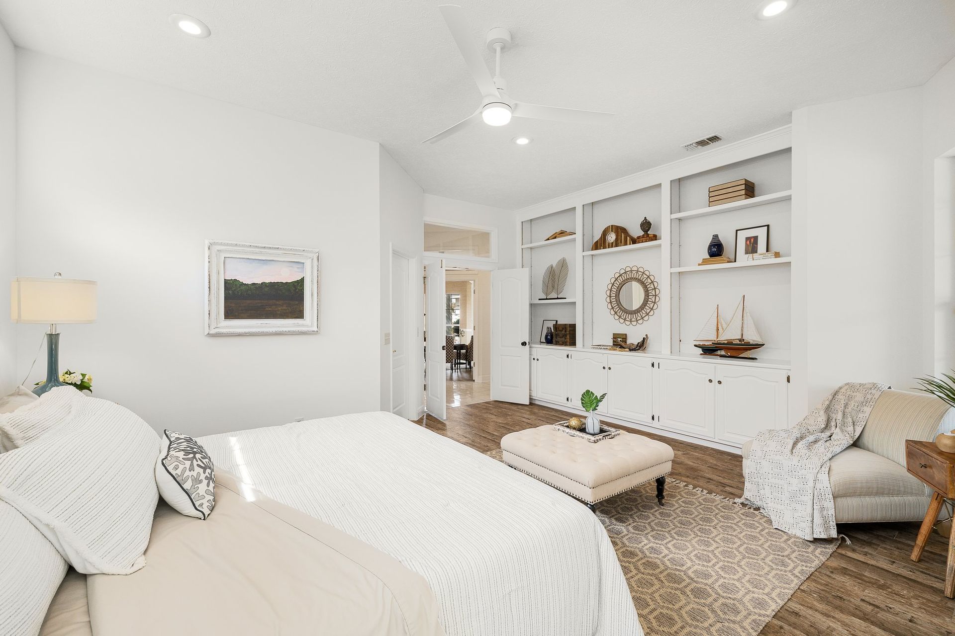 Bright white bedroom with a bed, armchair, bench, and built-in shelving in a coastal style