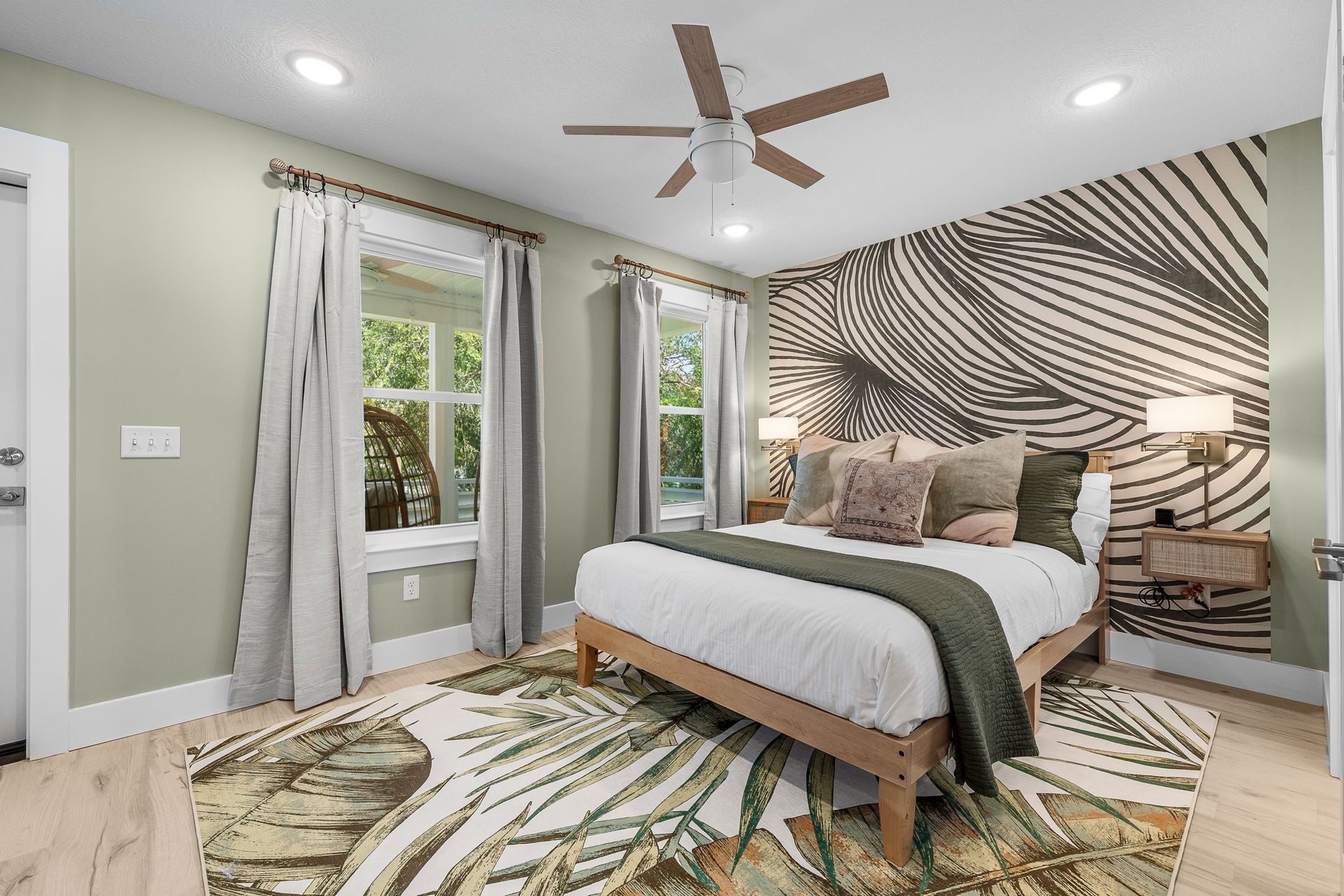 Bright bedroom with palm-print rug, striped accent wall, king bed, ceiling fan, and sliding glass doors
