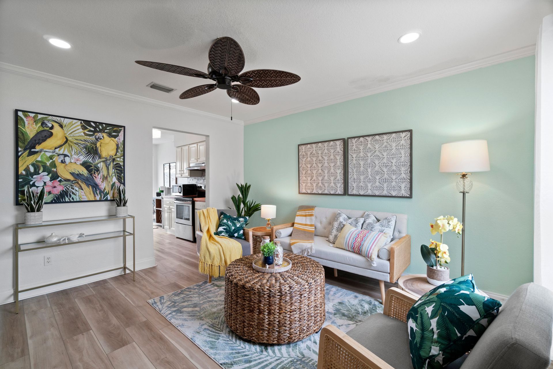 Bright living room with mint walls, wicker coffee table, white sofa, art, and ceiling fan.