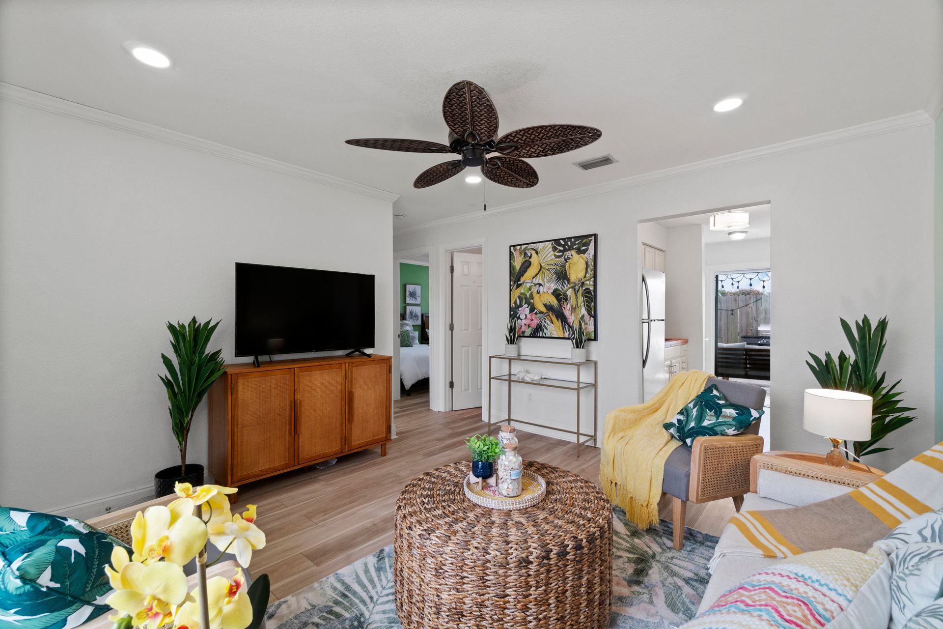 Bright living room with TV, wicker table, patterned sofa, plant, and ceiling fan