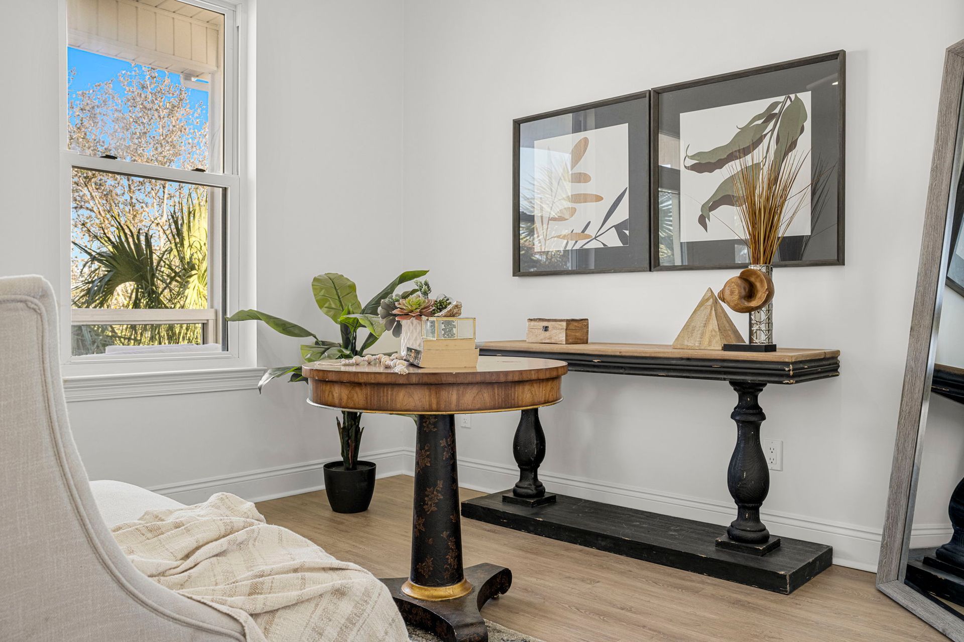 Bright home office with round wooden table, black console, window, and framed wall art